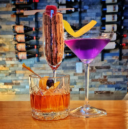 Three happy hours cocktails on a counter with wine bottles in the background.