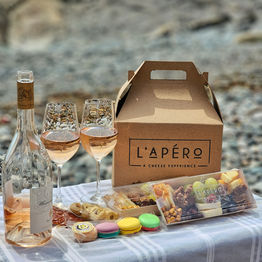 A Picnic Box on a beach with a sandwich, a cheeseboard, macarons and a bottle of wine with two glasses for lunch or dinner.