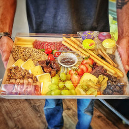 Person holding a Cheese Board , Charcuterie Board to go . Order online is available.