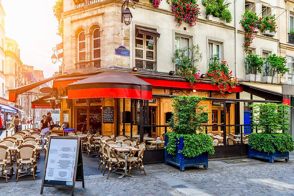 Terrasse d'un café parisien aux chaises en rotin, sous les géraniums d'une façade à volets