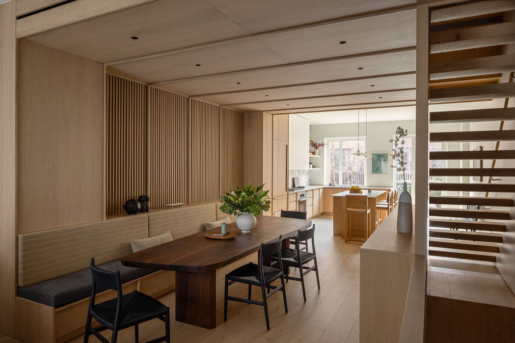 View of dining room into kitchen. Custom banquette and dining table. Oak wrapped architecture. Strong lines and soft colors. Designed by Emily Lindberg Design