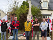 Five people in a line, standing in front of a Village War Memorial on Armistice Day