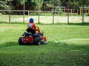 Commercial riding lawn mower, string trimmers, leaf blowers, and fuel cans neatly loaded on a utility trailer at a job site.