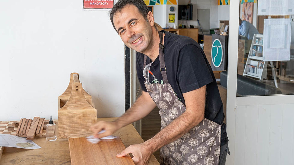 Man smiling while applying finish to a handcrafted wooden board at The Makers Society