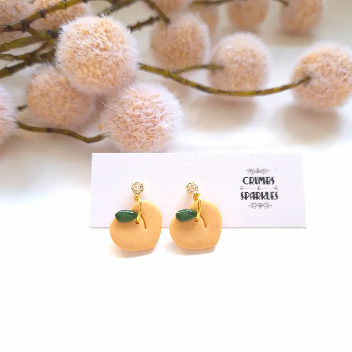 Peach earrings displayed on Crumbs & Sparkles branded card with fuzzy florals in background