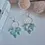Thumbnail: Close-up of geometric blue marbled earrings on gold hoops, handcrafted from polymer clay, displayed on white surface