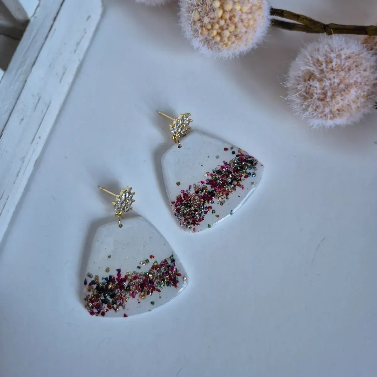 Handmade rainbow glitter statement earrings with gold crystal studs on white background, clay and resin dangle earrings