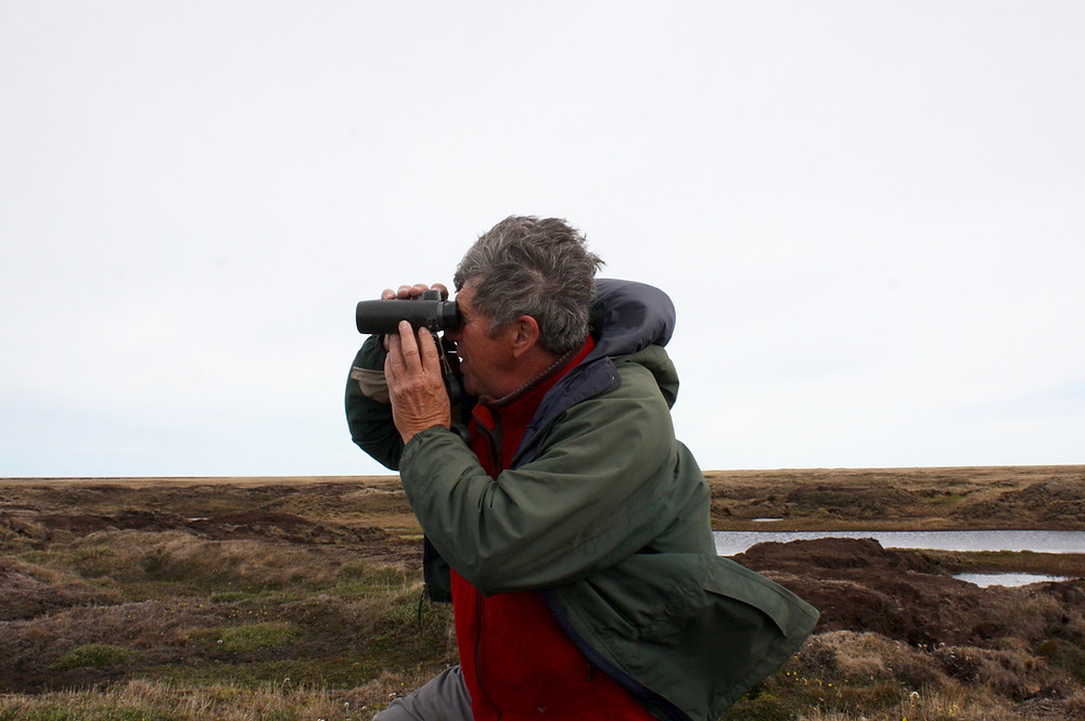 A man kneeling on the ground looks through binoculars.