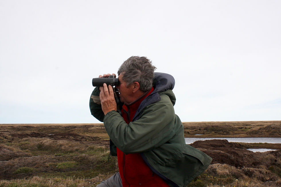 A man kneeling on the ground looks through binoculars.