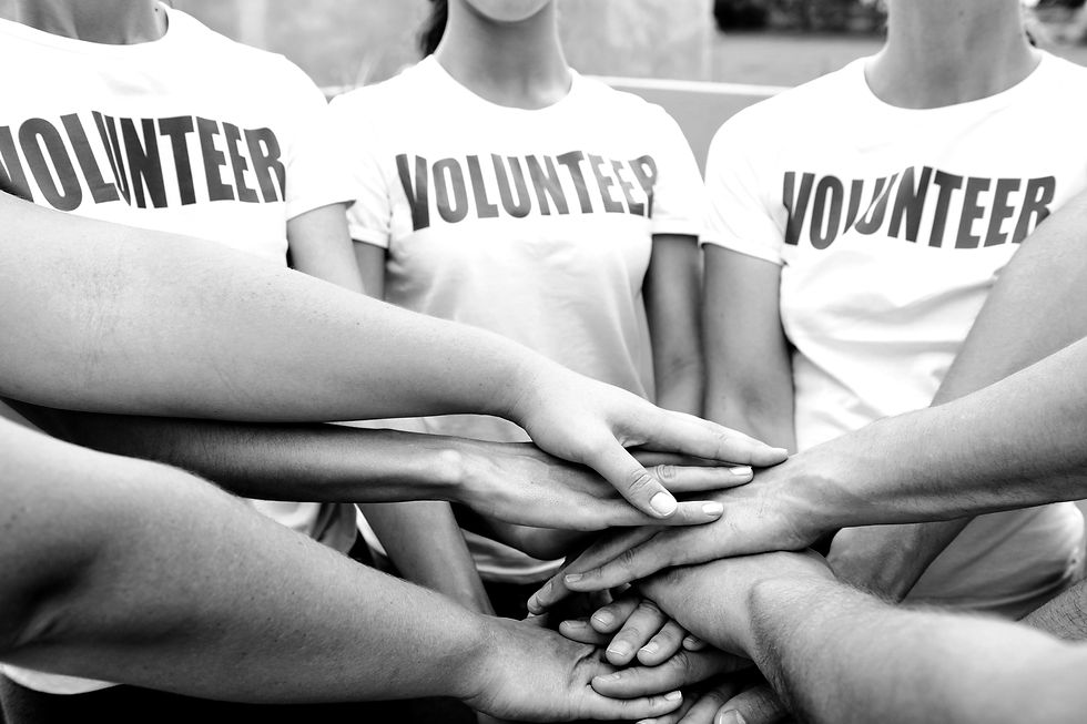 Group of people in "VOLUNTEER" shirts stack hands in unity. Black and white image conveys teamwork and solidarity.