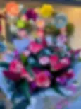 Un bouquet de roses roses bordées de blanc, de lys roses et de petites fleurs violettes, enveloppé dans du papier blanc.