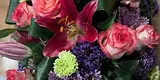 Un bouquet de fleurs roses, un lys pourpre, des œillets verts et des petites fleurs bleues.