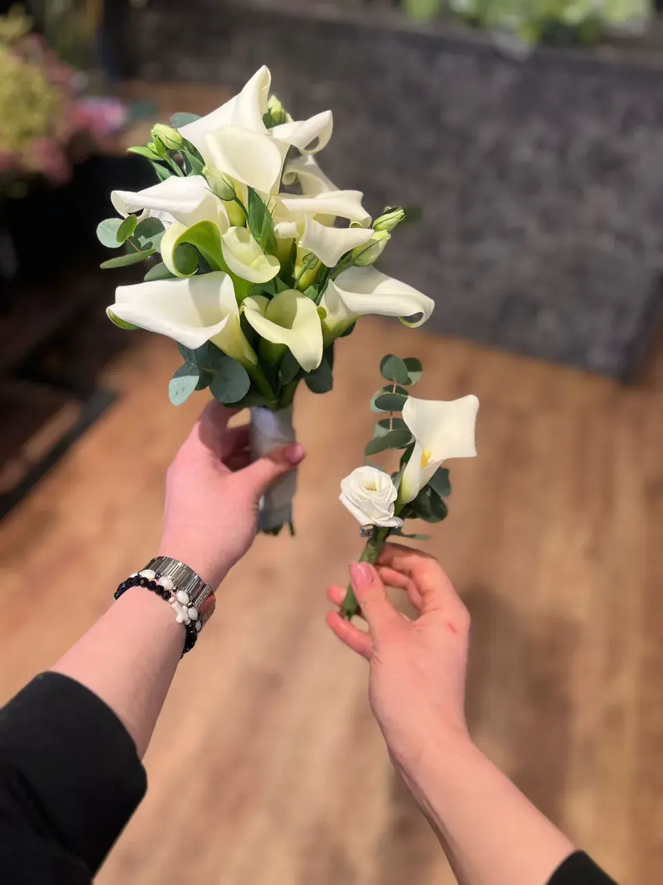 Mains tenant un bouquet évasé de callas blancs et un boutonnière assortie, décorés de feuilles d'eucalyptus.