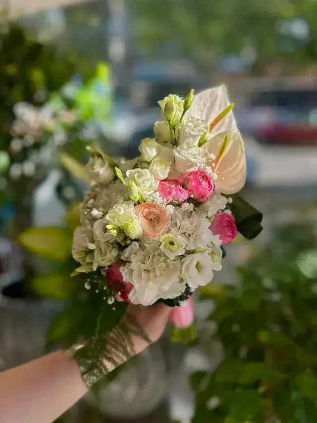 Un bouquet de mariée composé de roses roses et blanches, d'anthurium de couleur crème et de petites fleurs blanches.