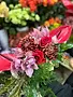 Gros plan d'un bouquet de fleurs composé d'anthuriums rouges vifs, roses rouges, chrysanthèmes bordeaux et orchidées roses avec des feuillages verts.