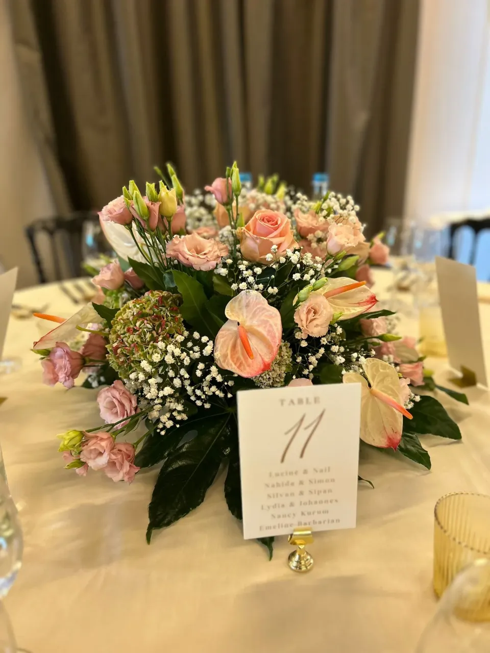 Vue de près d'un centre de table fleuri rose et blanc sur une table de mariage, avec une carte indiquant 'TABLE 11' et une liste de noms.