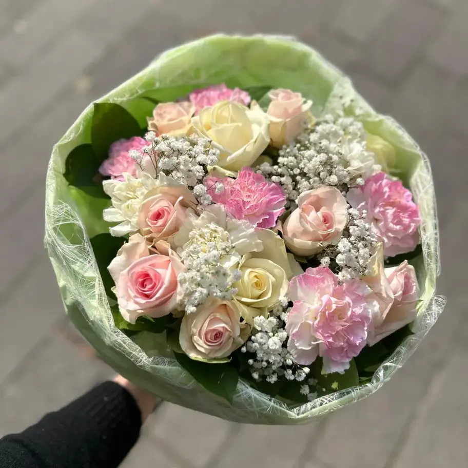 Un bouquet de roses et d'œillets roses et blancs, entouré de gypsophile et d'un emballage vert.