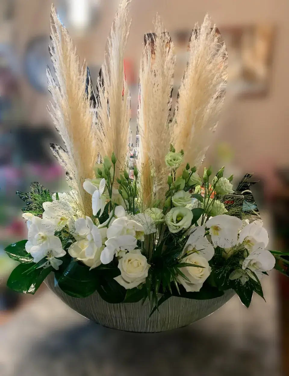 Composition florale moderne avec orchidées blanches, roses, feuillage vert dense et herbes de la pampa séchées.