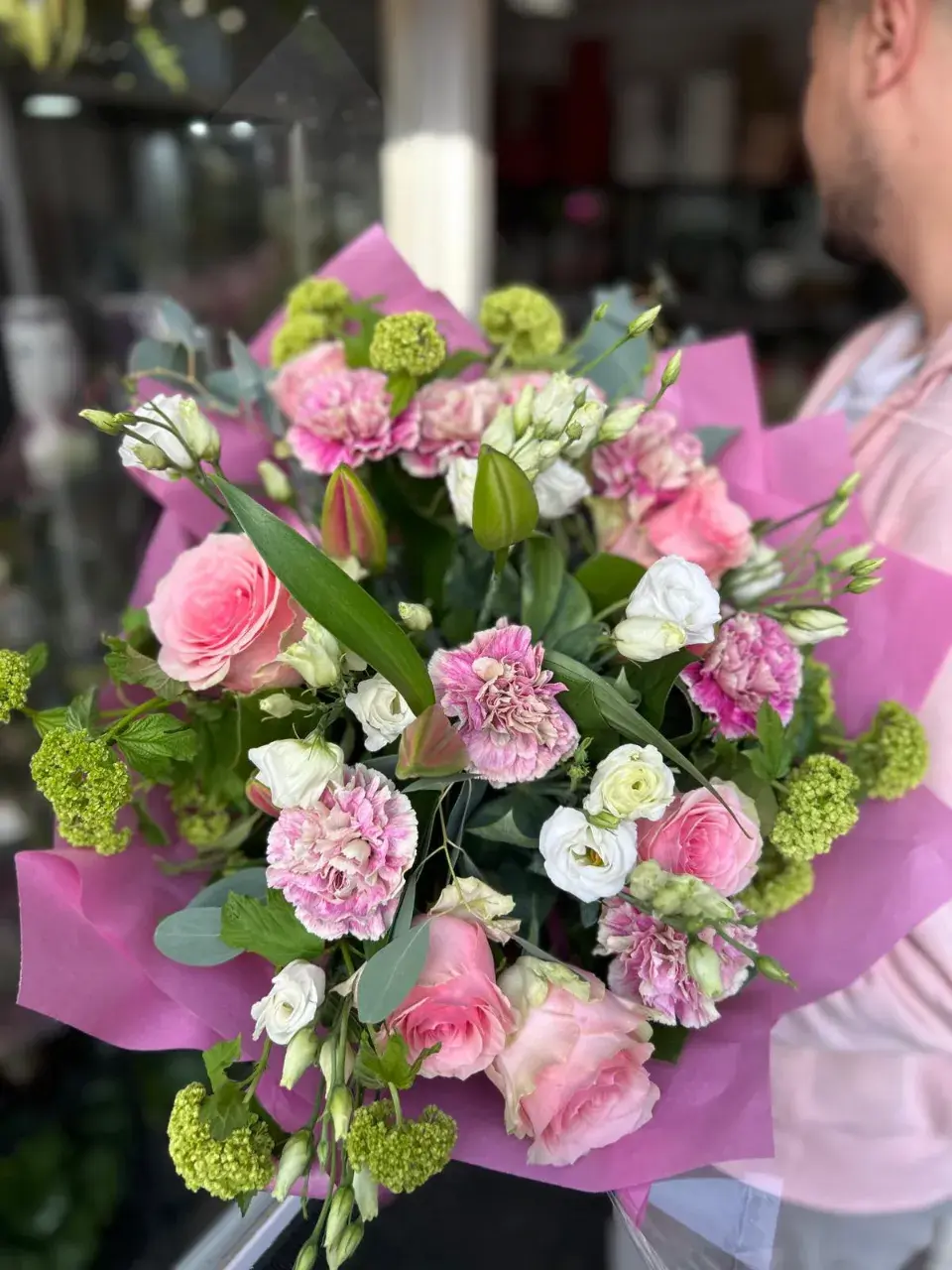 Un bouquet de fleurs aux tons rose pâle et blancs, composé de roses, d'œillets et de petites fleurs d'hortensia vertes.