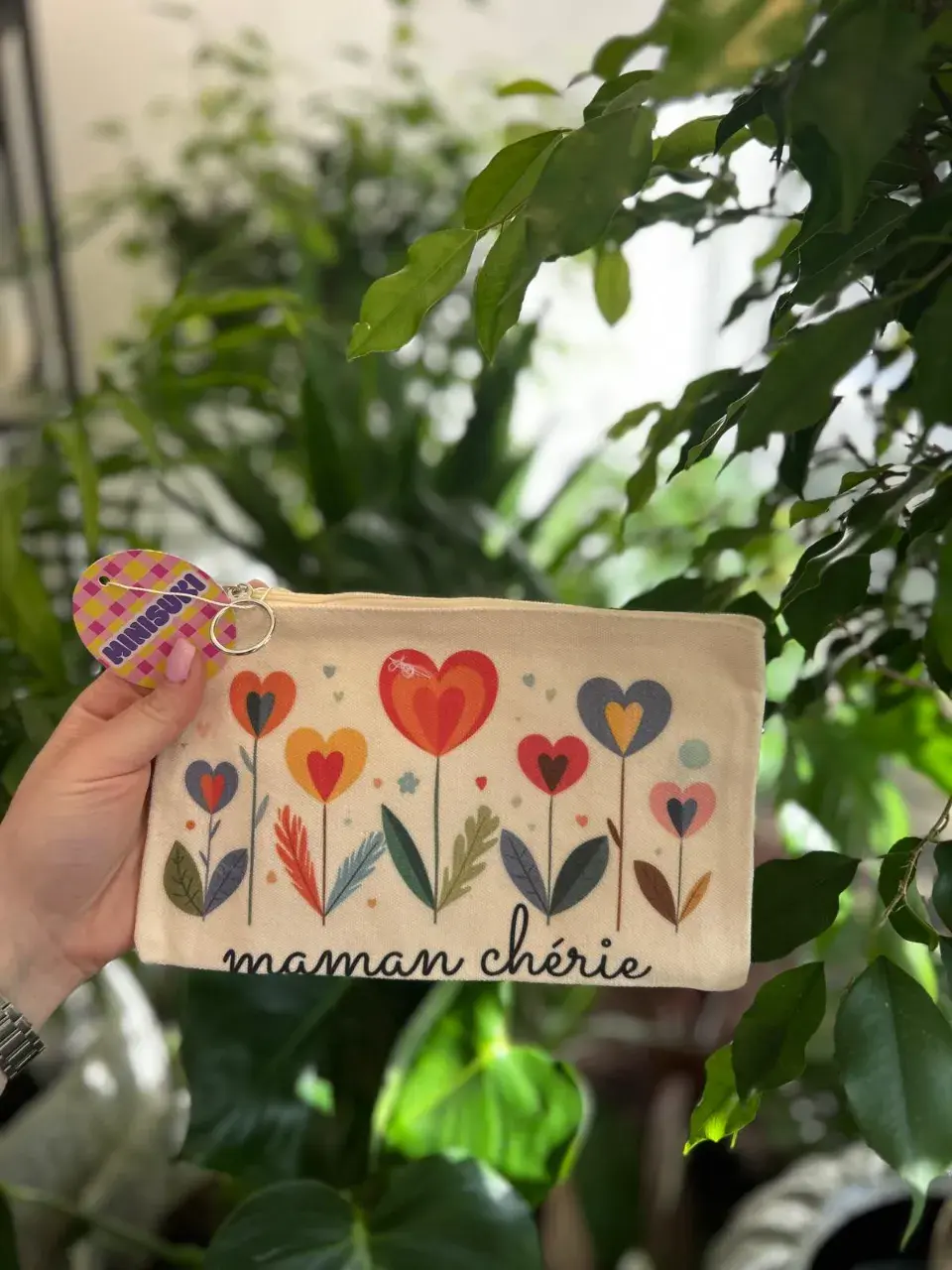 Une trousse décorée de fleurs en forme de cœur et inscrite « maman chérie », tenue par une main.