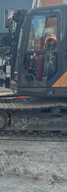 Excavator digging trench for drain installation in urban area.