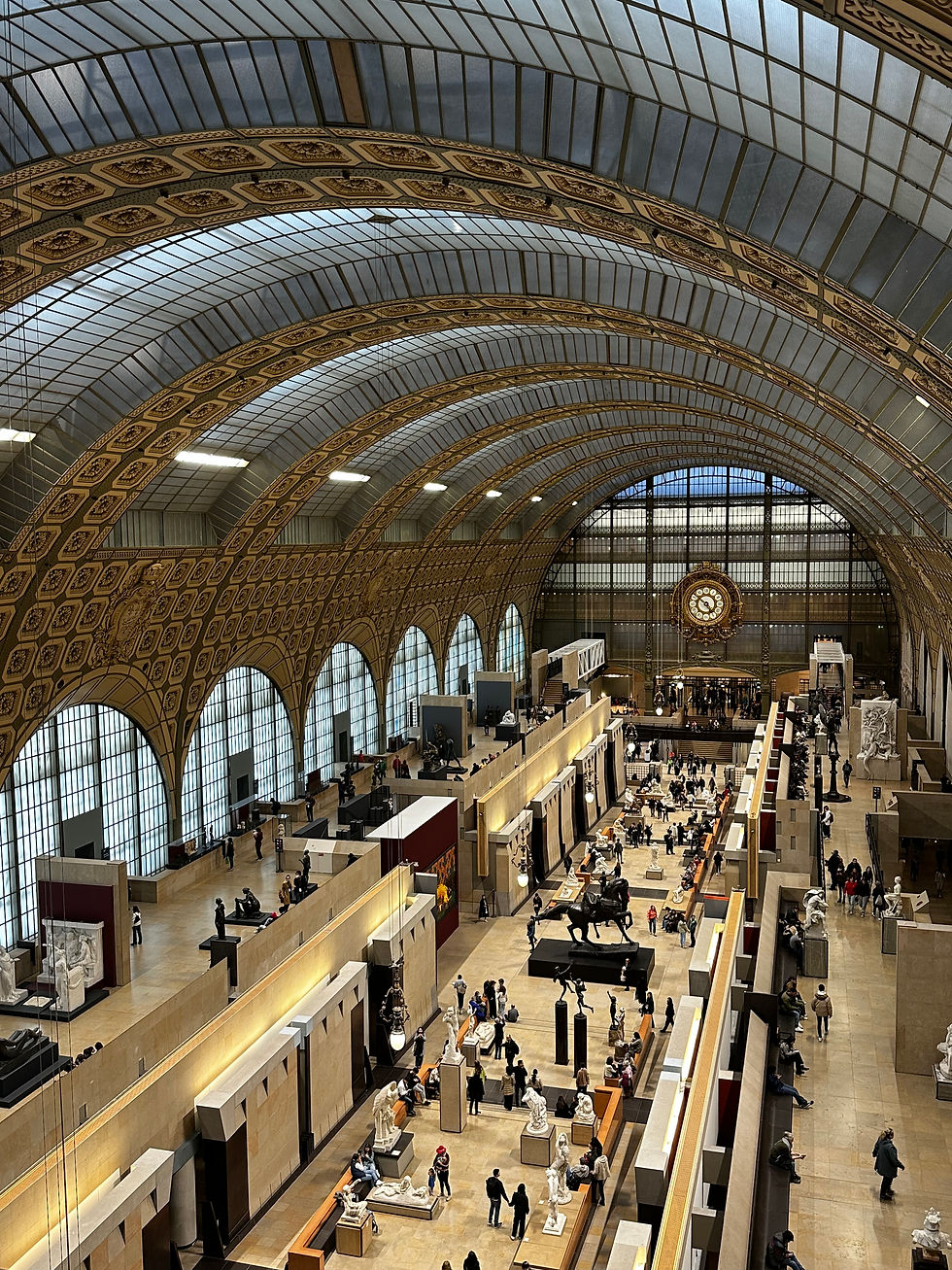 Grand museum hall with arched glass ceiling, giant clock, sculptures, and visitors browsing exhibits under soft light.