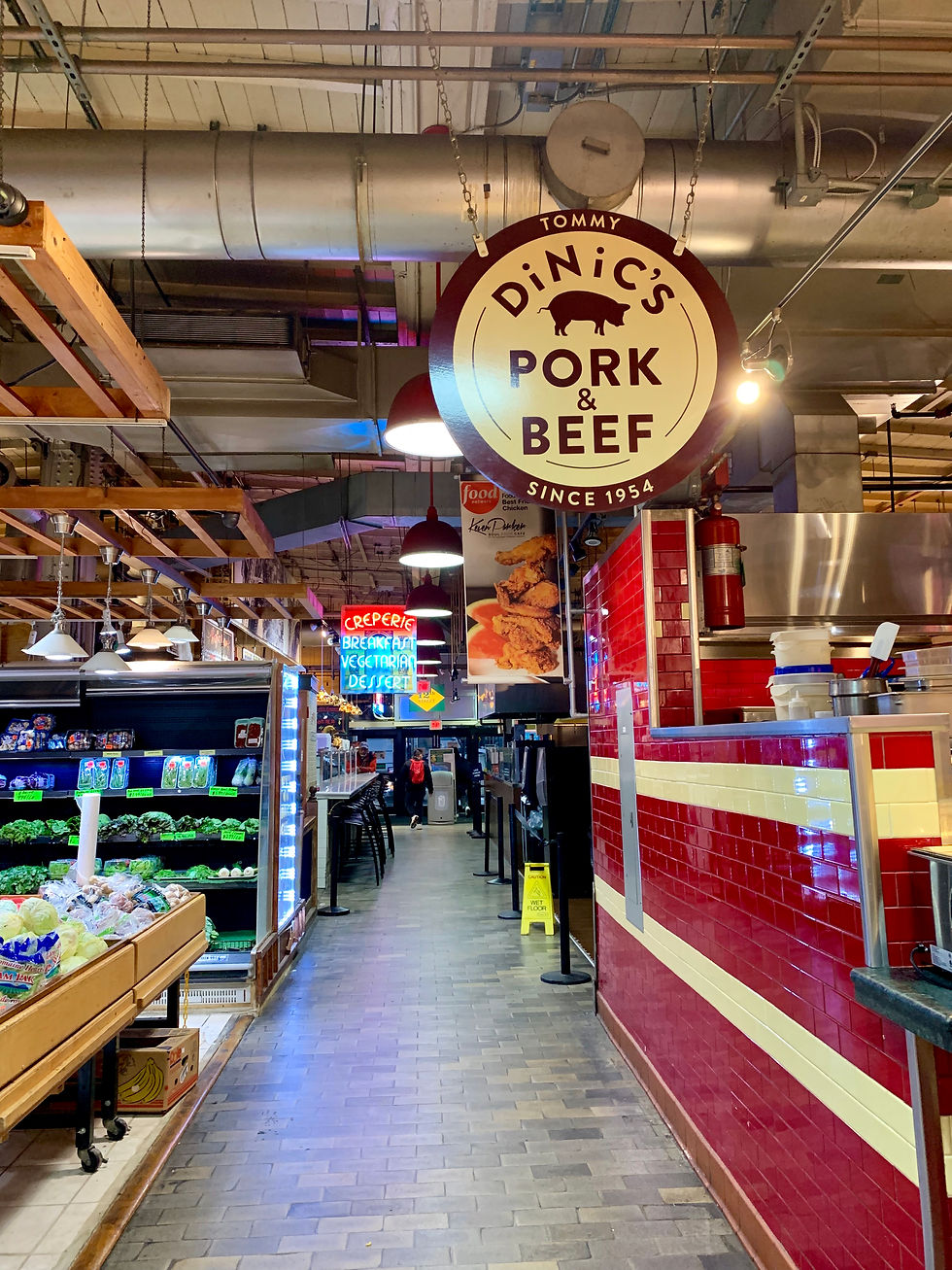 Indoor market aisle with hanging DiNic’s Pork & Beef sign, red tiled counter, produce shelves, and neon food signs under industrial pipes