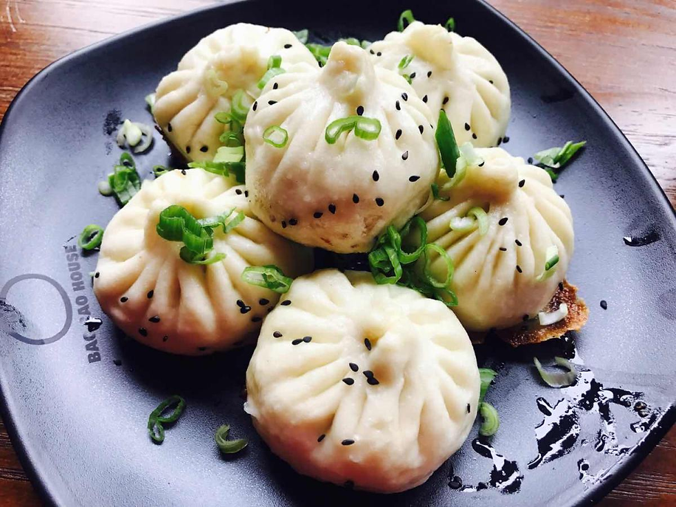 Steamed bao dumplings topped with sesame and green onions on a black plate, with BAO HOUSE text visible.