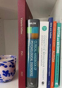 a selection of different coloured psychology text books including a thesis to the right next to a speckled blue candle.
