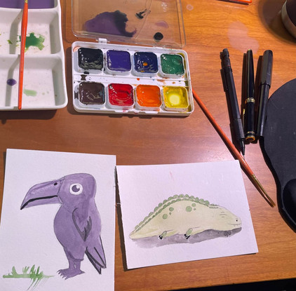 There are two paintings on the table with a palette, pens and paint brushes. The painting shows a purple and a green crocodile.