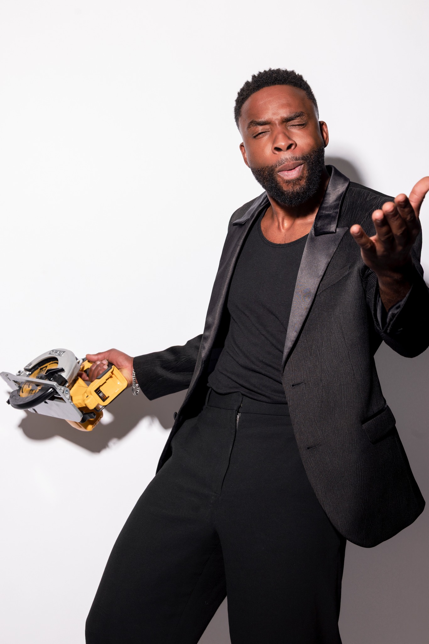 Thomas Copeland Jr. in a black suit holding a yellow circular saw against a white background