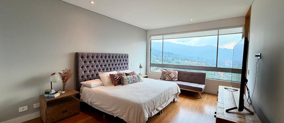 Alcoba principal con piso en madera, cabecera tapizada y ventanal con vista a la ciudad, arriendo Los Balsos