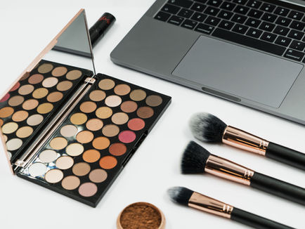 Makeup products beside a laptop, representing the creator economy behind Get Ready With Me videos
