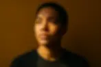 Young adult standing before a bold background with soft light, symbolizing seeking and finding salvation through Christ