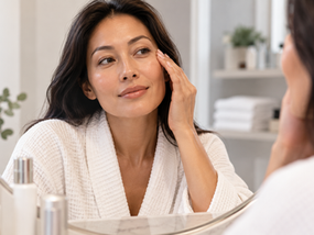 Woman examining natural skin quality in a softly lit skincare setting