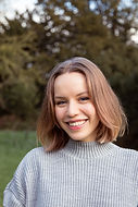 Smiling young woman wearing grey sweater, natural background, positive expression.