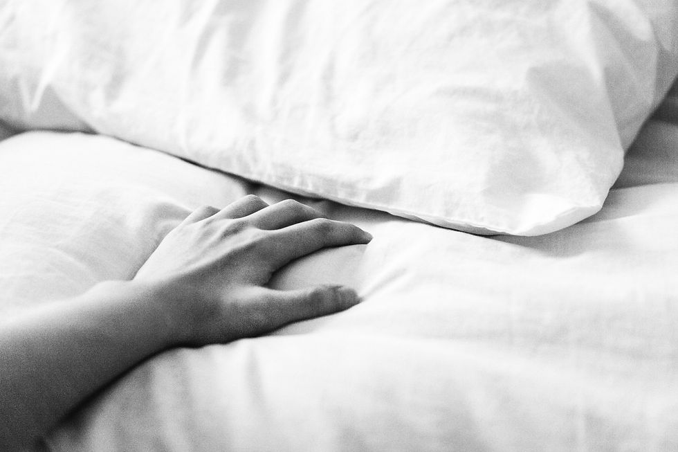 Black and white close-up of a hand resting on an empty side of the bed