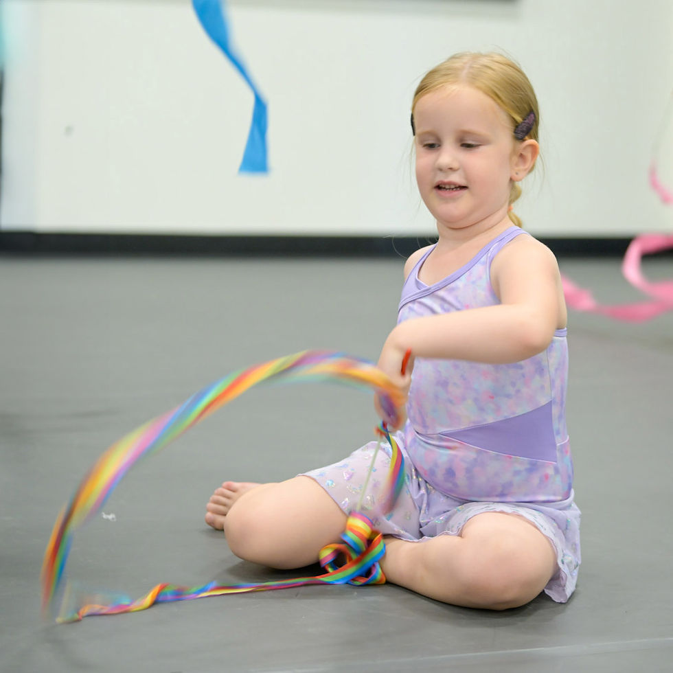 A girl in a purple leotard is sitting and twirling a ribbon.