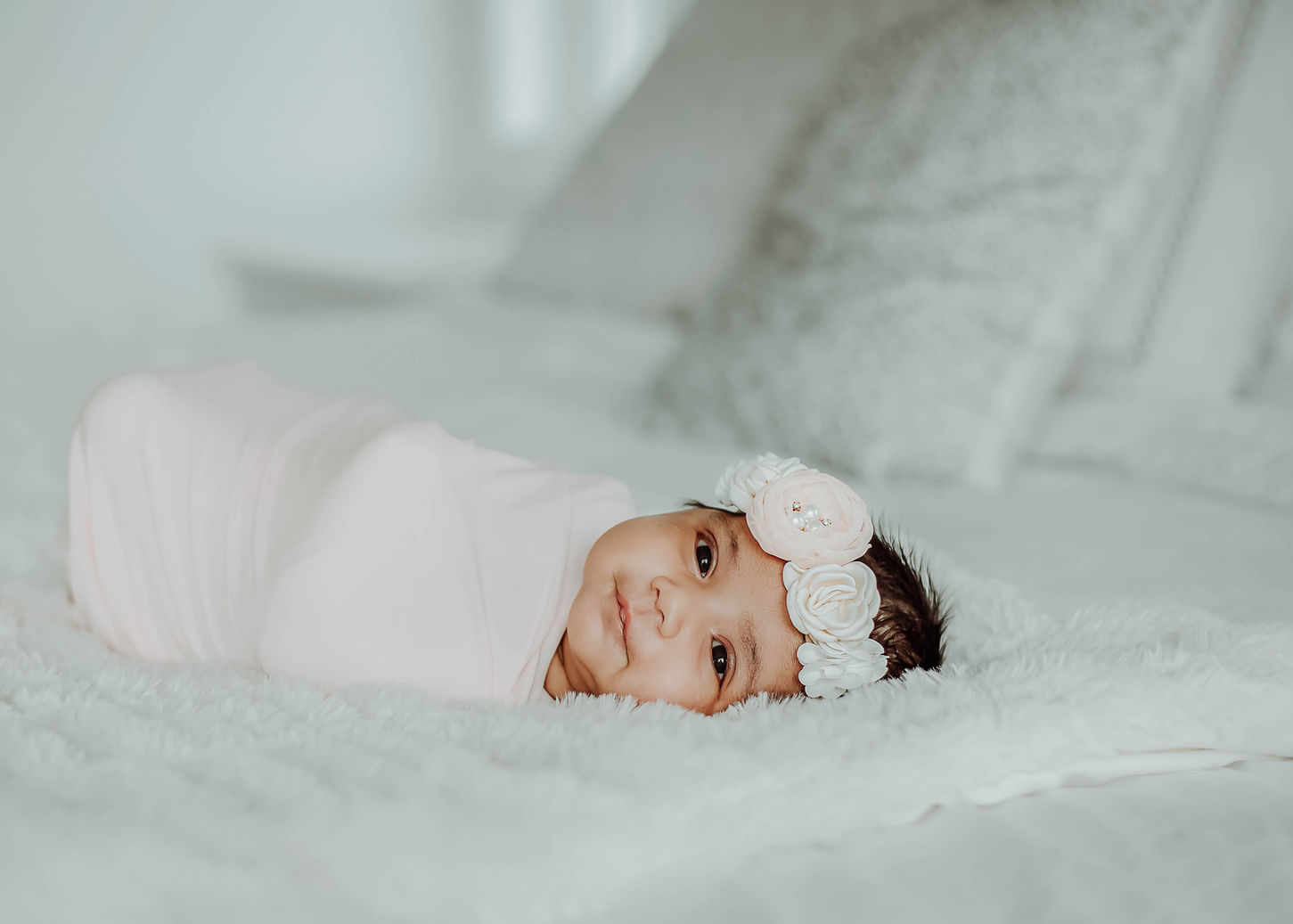 Baby girl laying on bed smiling.