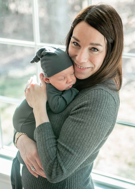 Mom holding baby in front of window.