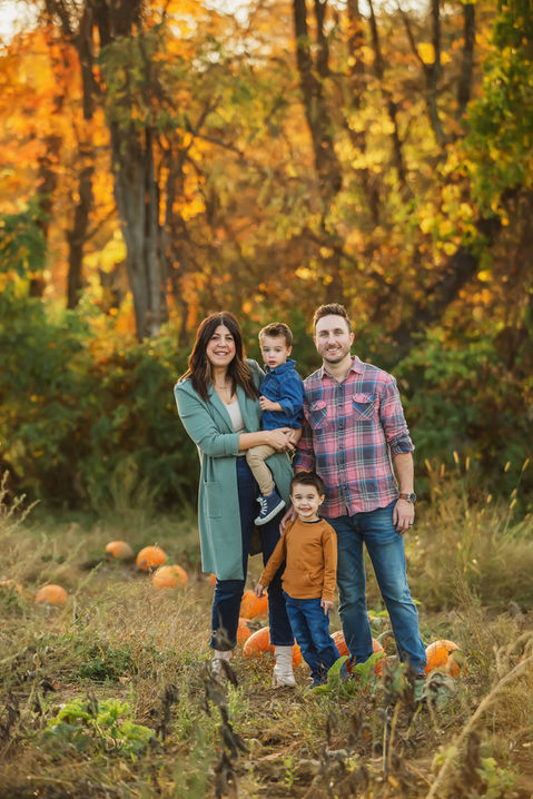 Mom holding son with dad and other son standing in a field of pumpkins.