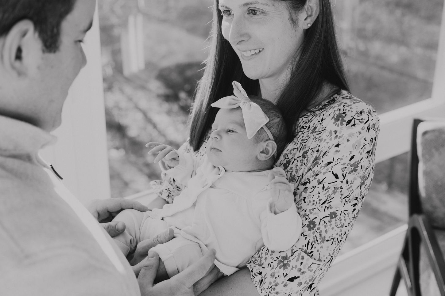Baby girl being held by mom and dad who are standing in front of each other. 
