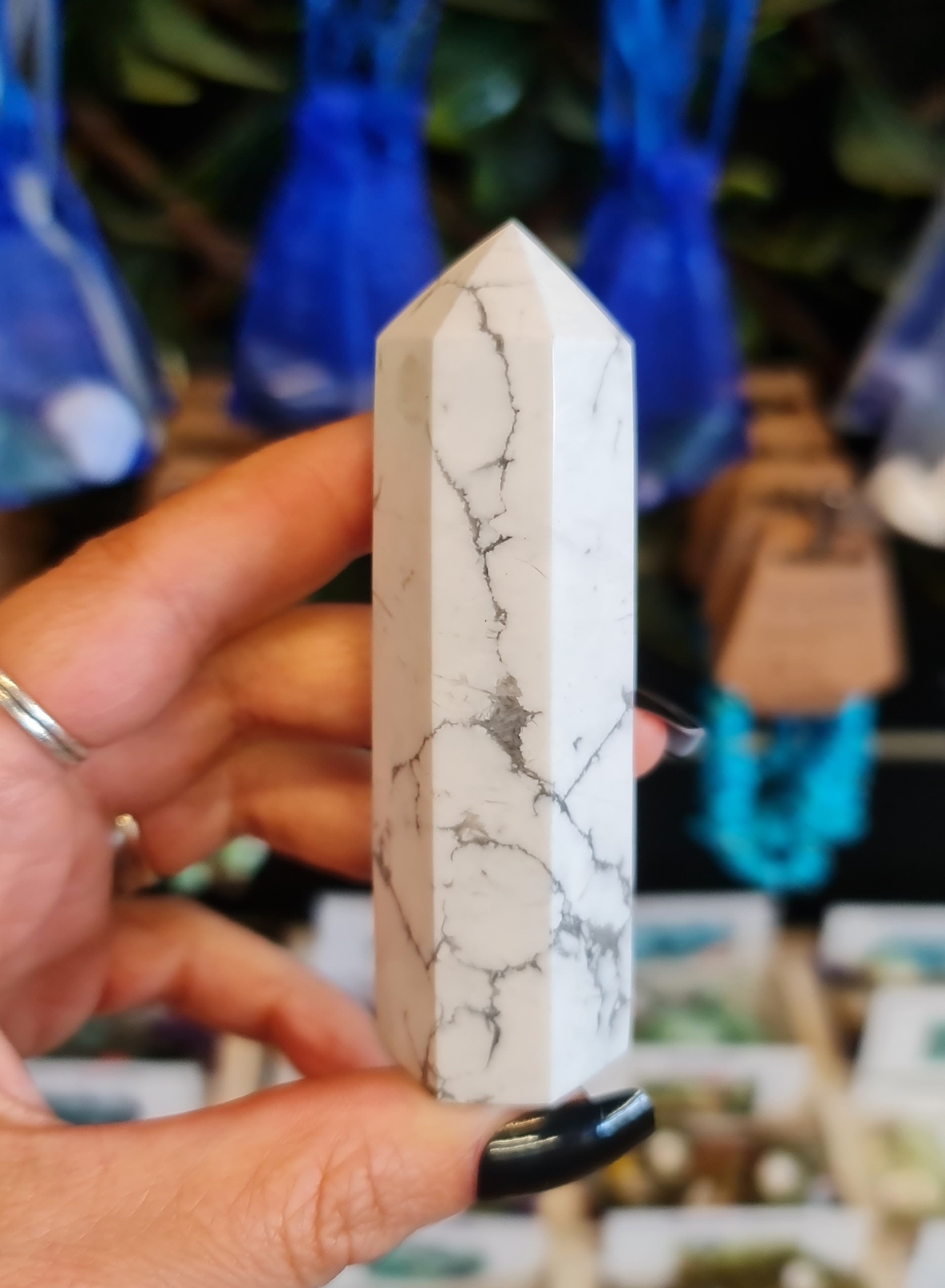 an image of a polished howlite tower with colourful bags and bracelets in the background
