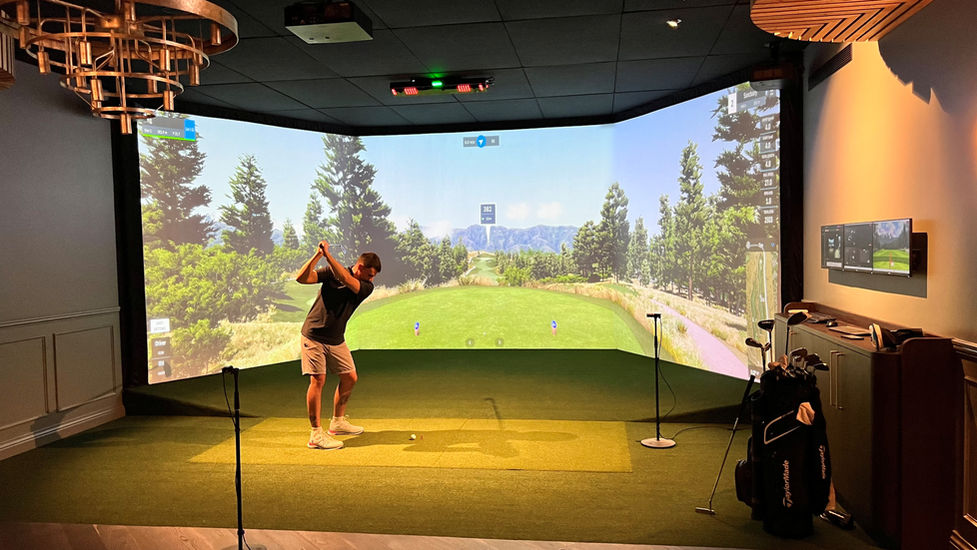 Golfer mid-swing inside luxury home golf simulator powered by GSPro and Uneekor, surrounded by high-end furnishings and launch data on screen.