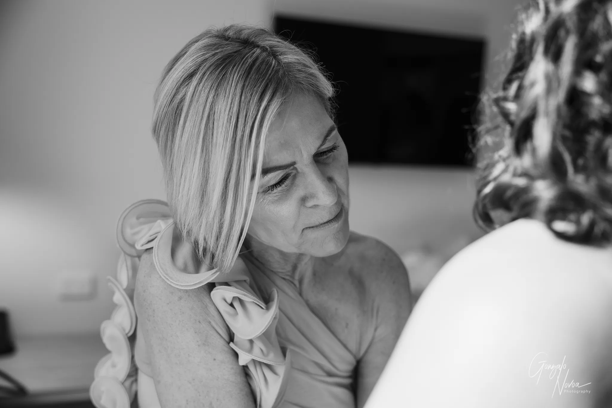 Black and white close-up of Tahnee’s mum focusing carefully as she helps button the back of Tahnee’s wedding dress, capturing a heartfelt and emotional moment before the ceremony.