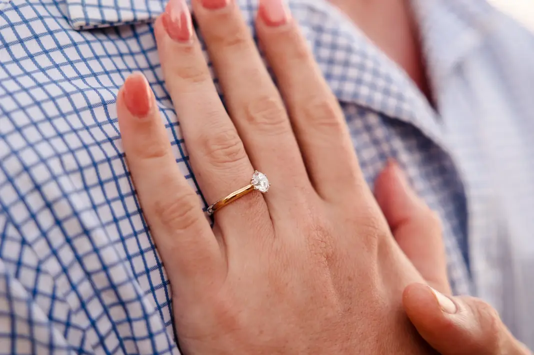 Close-up of Baleigh’s hand on Kailym’s chest, showcasing her gold engagement ring with an oval diamond.