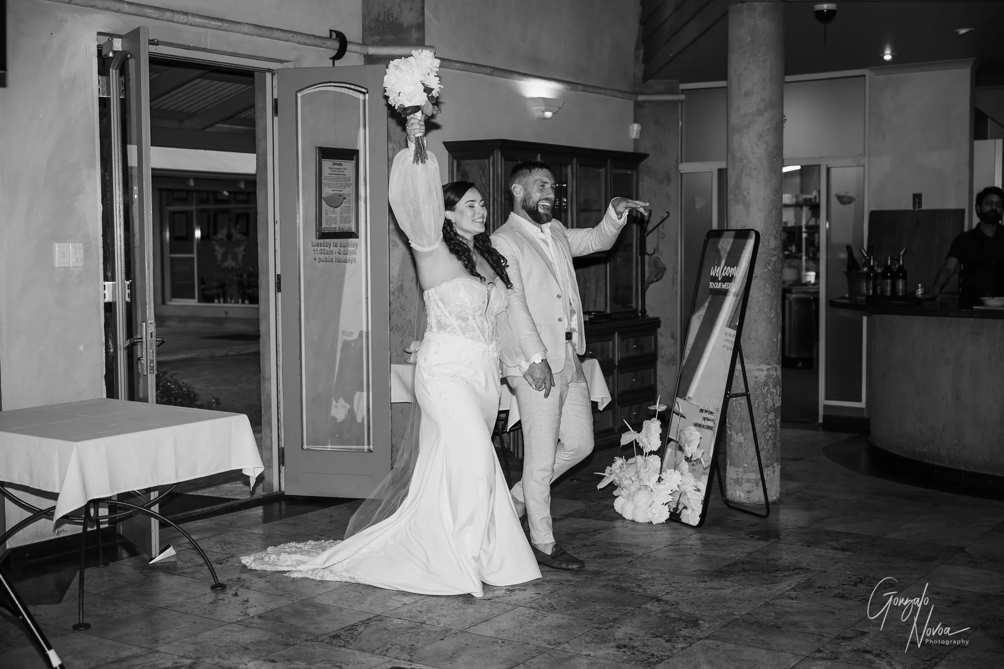 Bride and groom entering the reception with big smiles, bride raising bouquet in the air