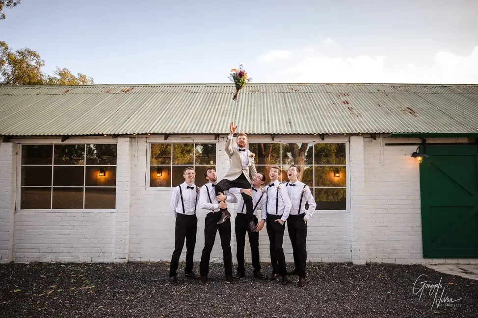 Groom being lifted by groomsmen while tossing a bridal bouquet at Mardella Meadows in WA.