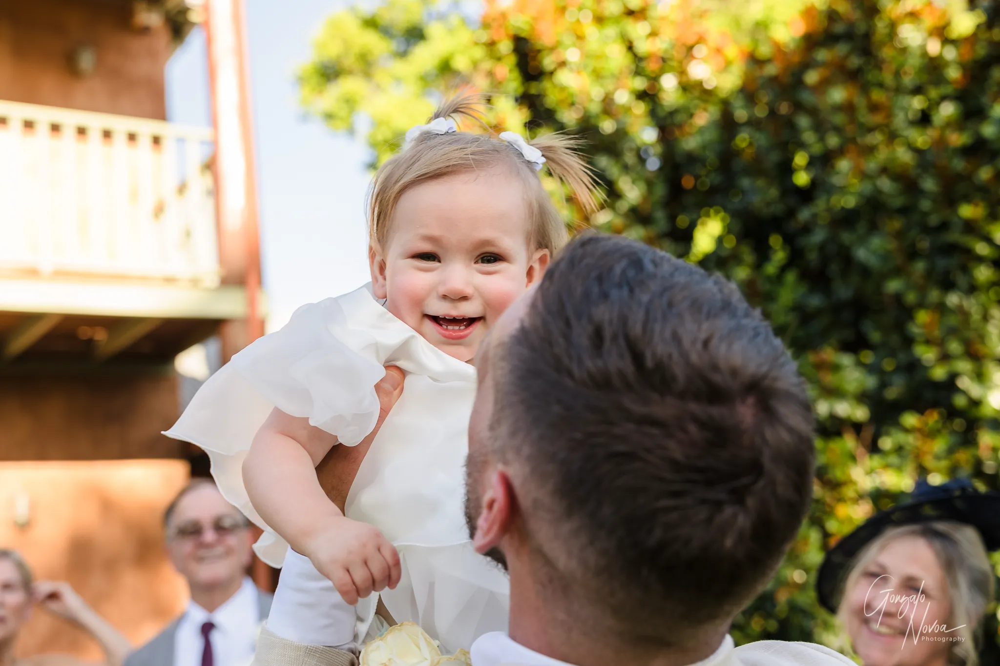 Close-up of little Arlea smiling brightly as her dad James holds her up during family celebrations at the wedding