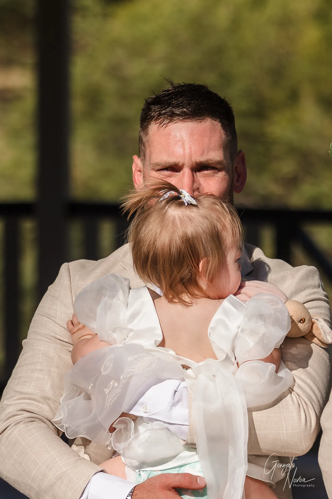 Groom James stands at the altar, eyes glistening, as he cradles his daughter Arlea tightly in his arms while waiting for Tahnee to arrive at their ceremony.